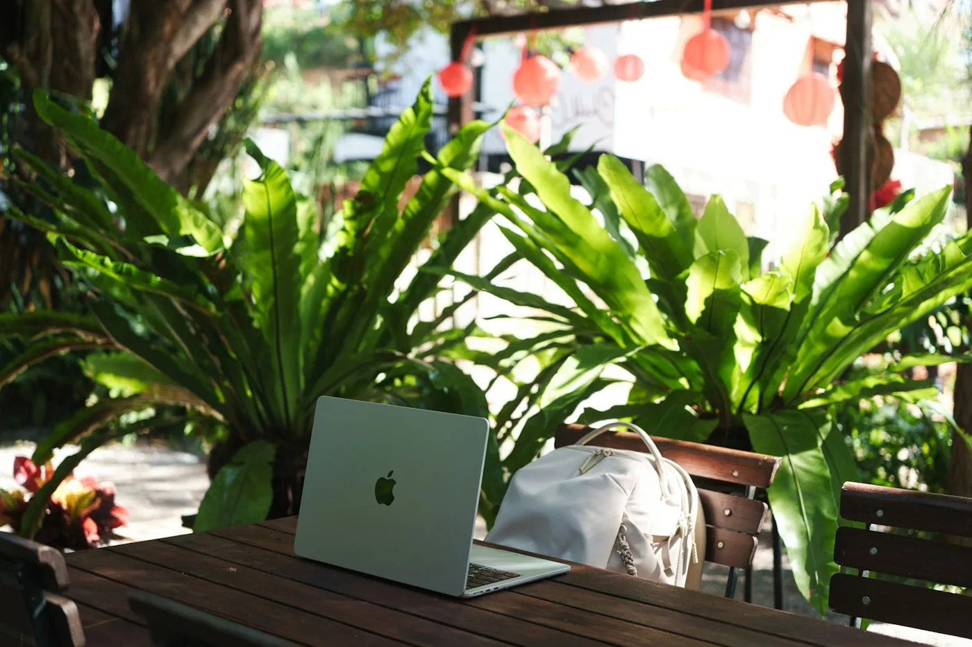 Laptop and backpack on a wooden cafe table among large green plants