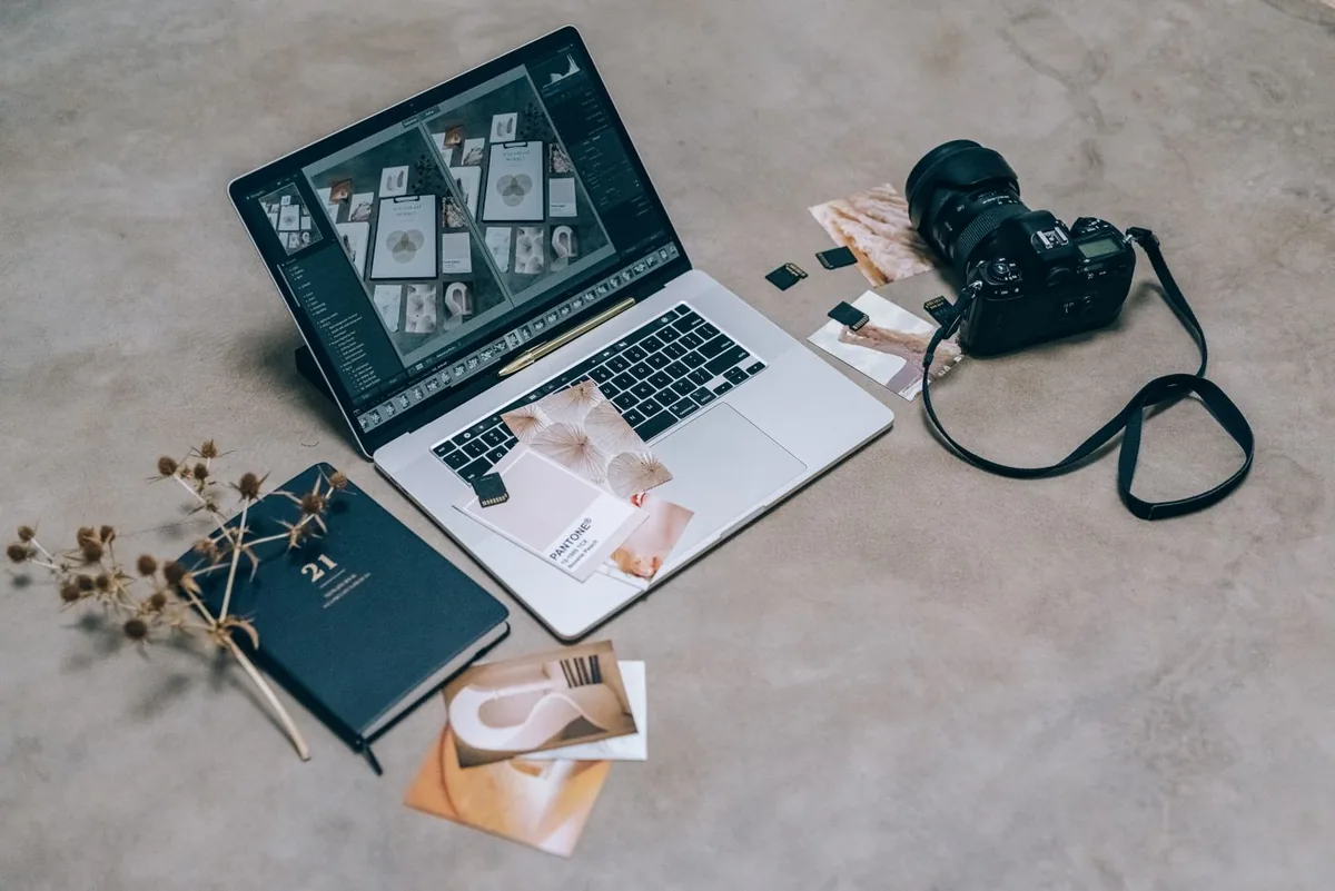 Laptop with a photo contact sheet open next to a camera and memory cards on a concrete floor