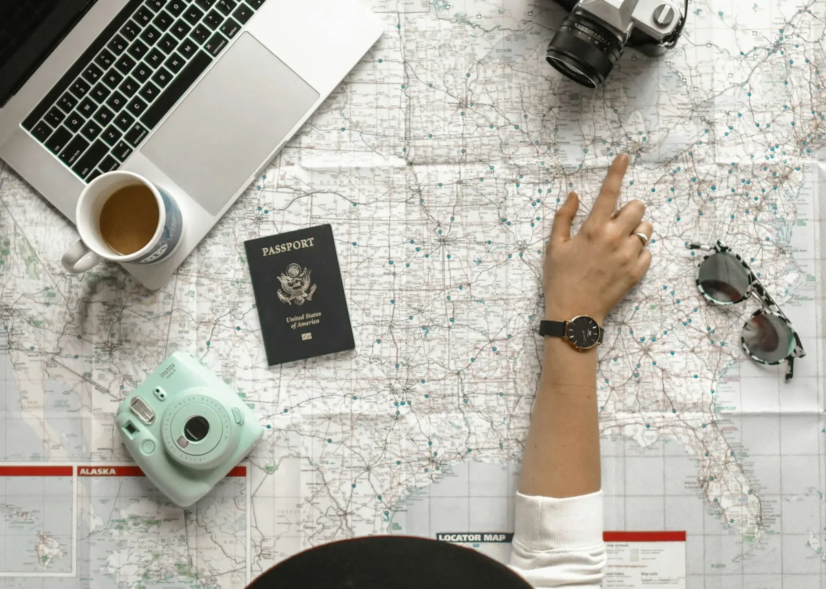 Laptop, camera and passport on a map with a hand pointing at the route