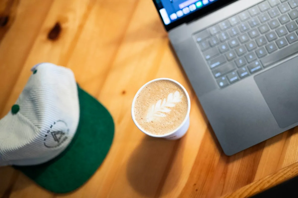 Laptop, Latte und eine Kappe auf einem Holztisch im Café