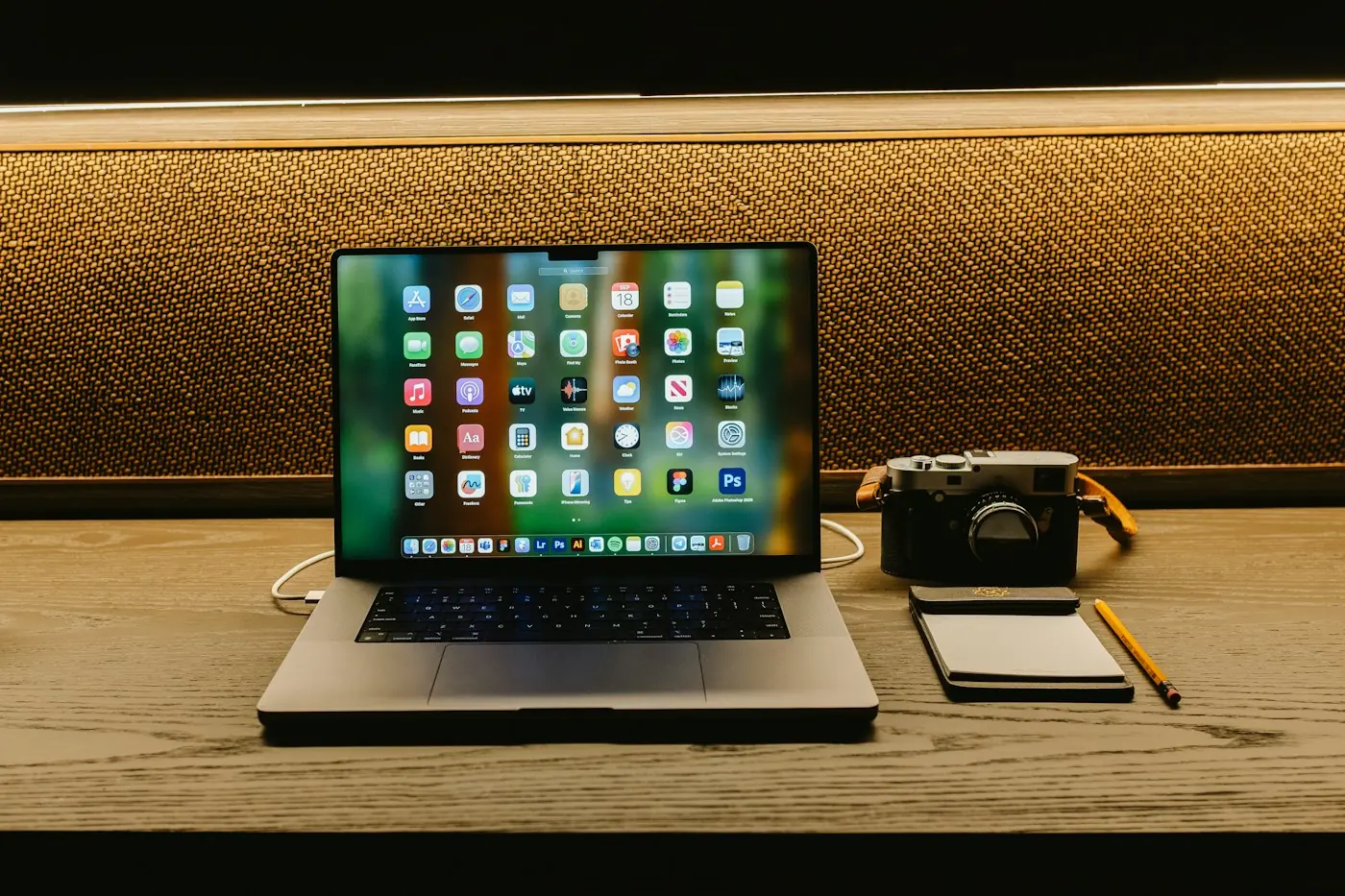 Laptop open next to a compact camera and a notepad on a wooden desk
