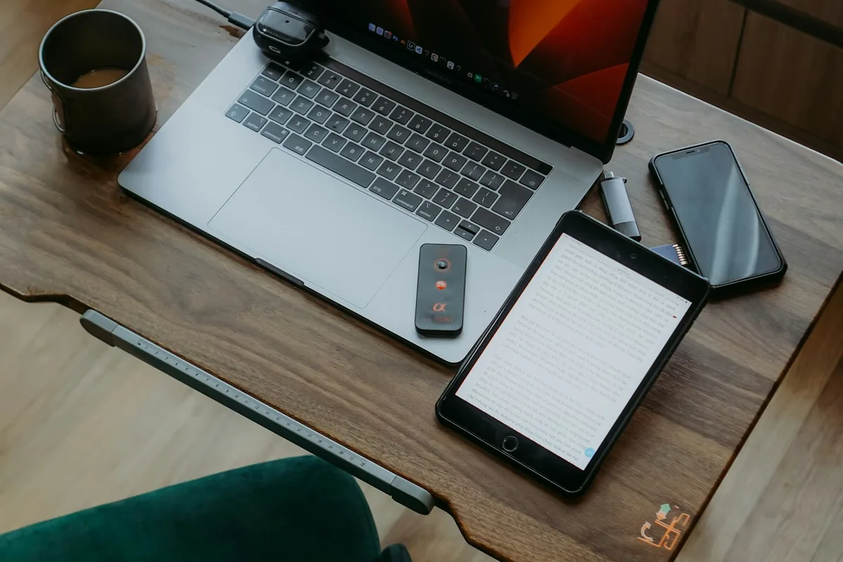 Een laptop, tablet en telefoon op een houten bureau met een afstandsbediening en een kopje