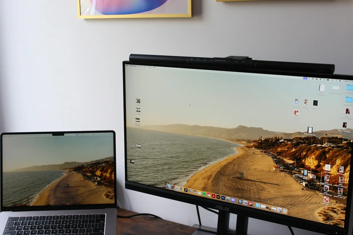 Laptop on a desk next to a large monitor showing the same beach picture