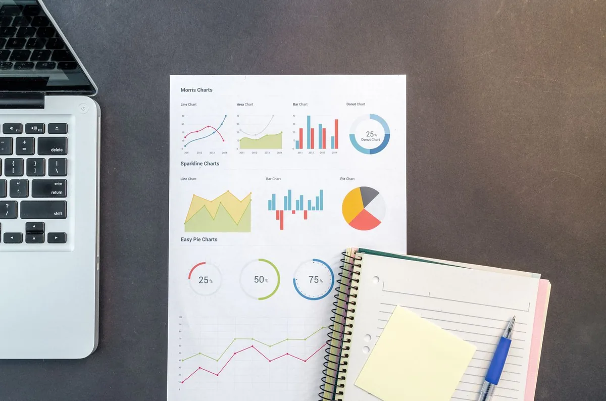 Laptop, notebook and printed charts on a desk, seen from above