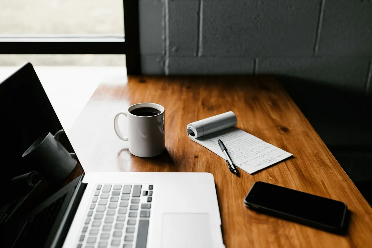 Laptop, notepad, mug and phone on a wooden desk