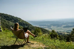 A woman in a camping chair working on a laptop above a green valley
