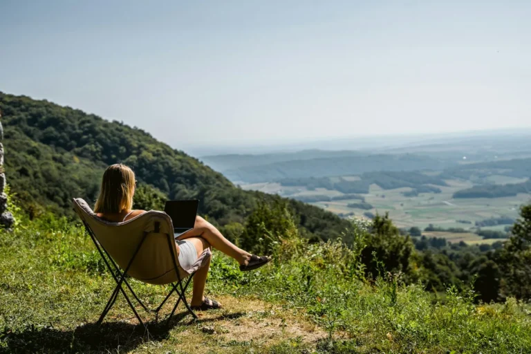 A woman in a camping chair working on a laptop above a green valley