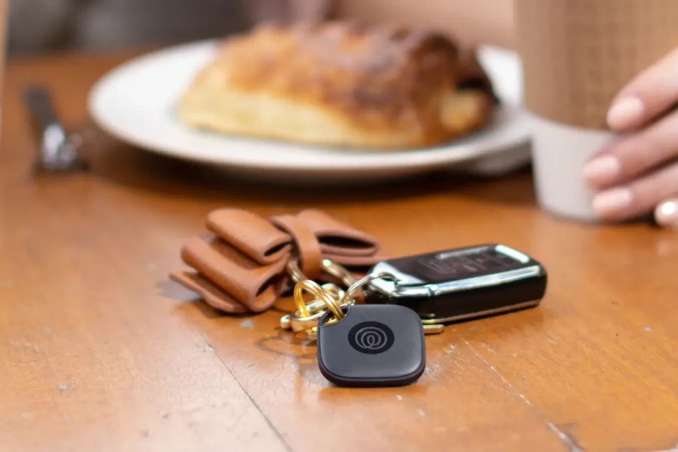 Black Tile tracker on a key ring lying next to a car key on a cafe table