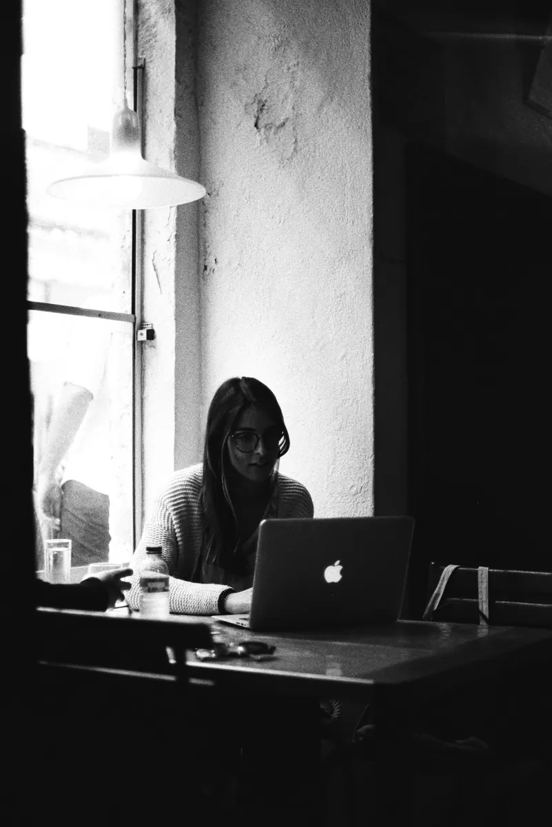 Woman working on a laptop at a table by a window