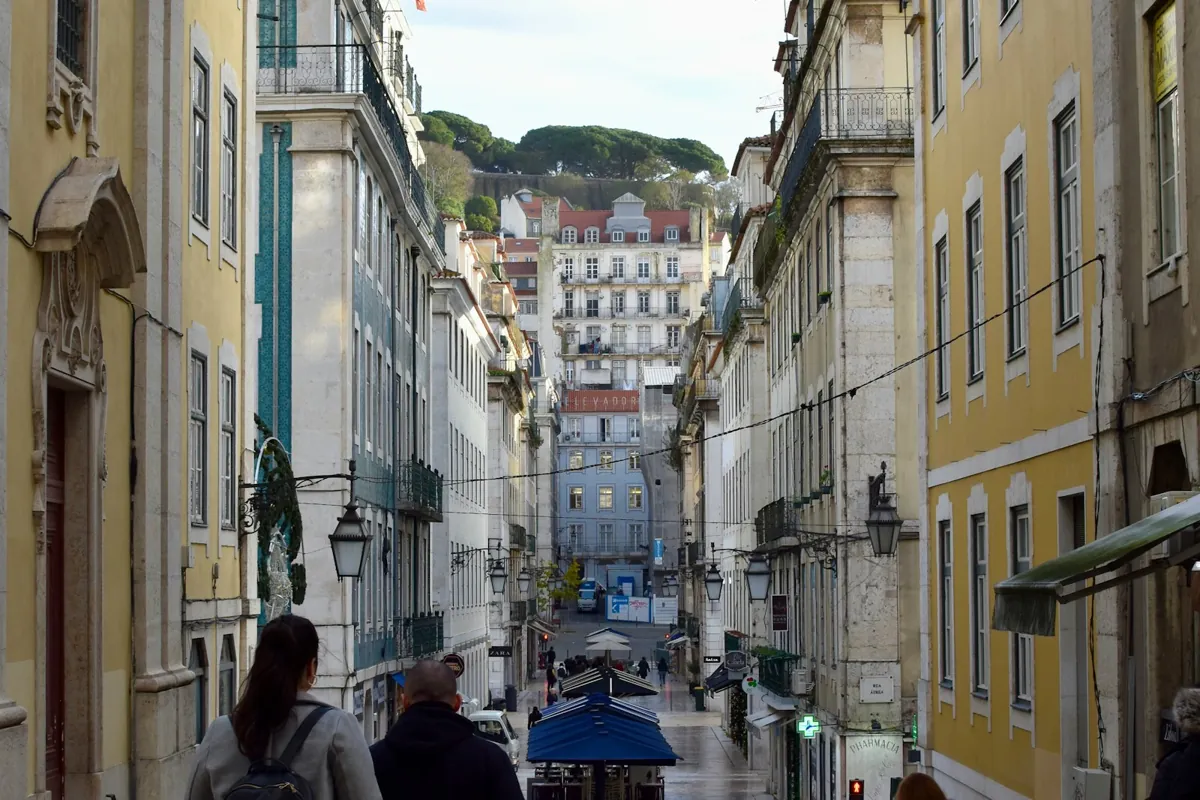 Two people walking up a steep Lisbon street between tall buildings