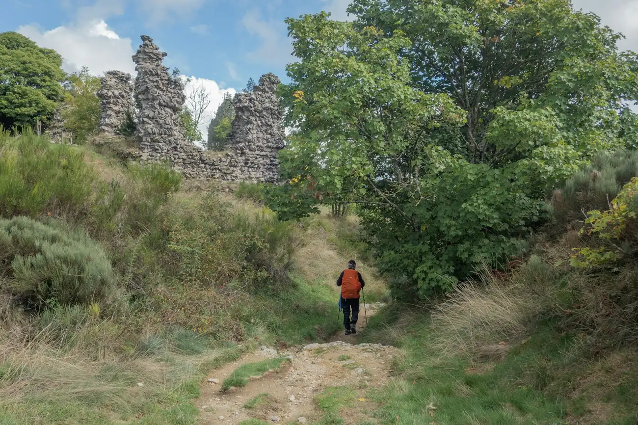 A lone hiker in an orange jacket walking a green path towards old stone ruins