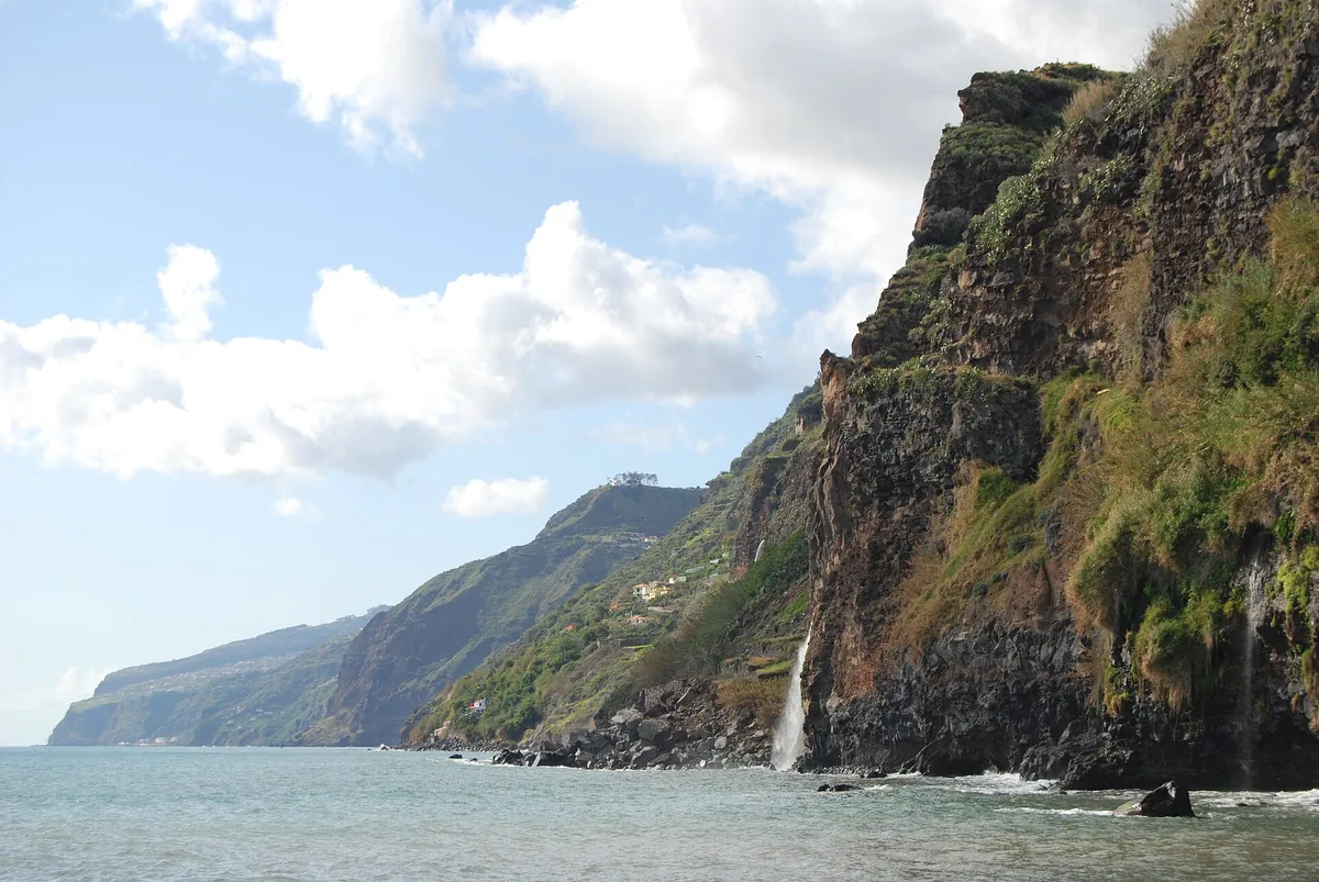Empinados acantilados verdes junto al mar cerca de Ponta do Sol, Madeira, con una fina cascada