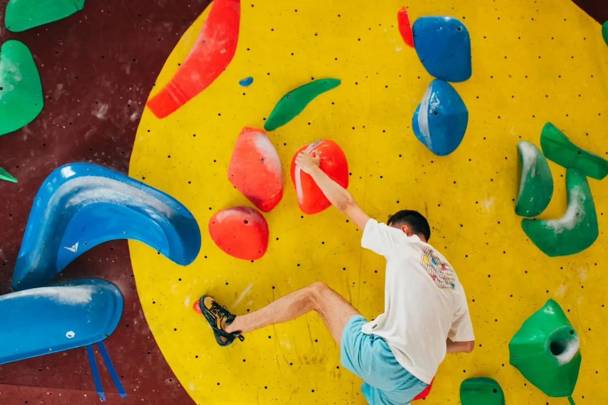 Man in a white t-shirt bouldering on a yellow indoor wall with colorful holds