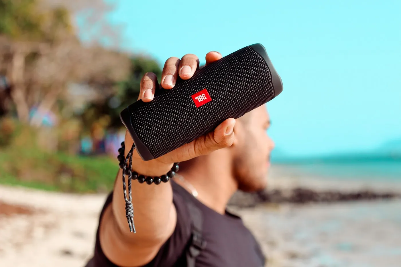 A man on a beach holding up a black JBL Bluetooth speaker