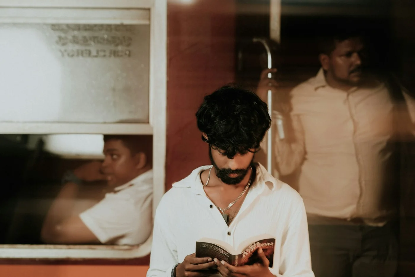 A man in a white shirt standing on a railway platform and reading a small book