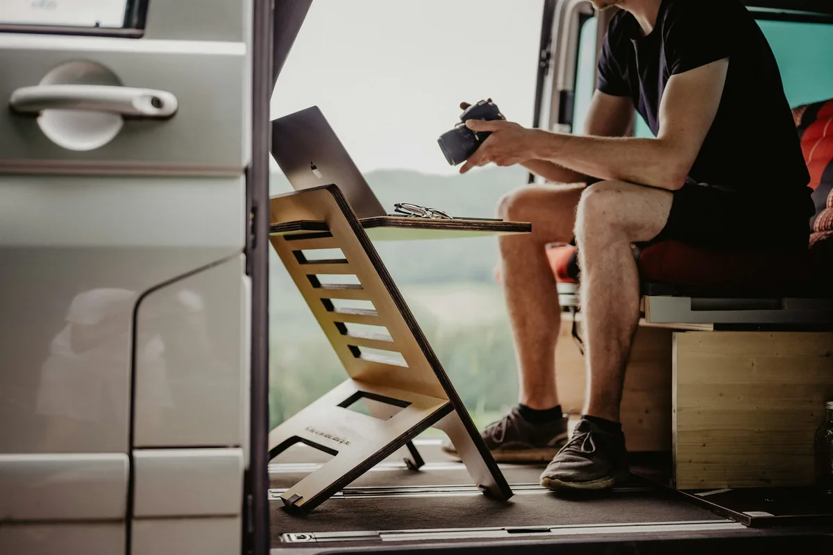 Een man werkt op een laptop op een standaard in de zijdeur van een camper