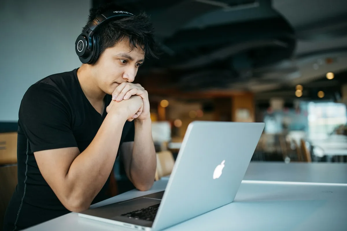 A man wearing black over-ear headphones working on a laptop at a table