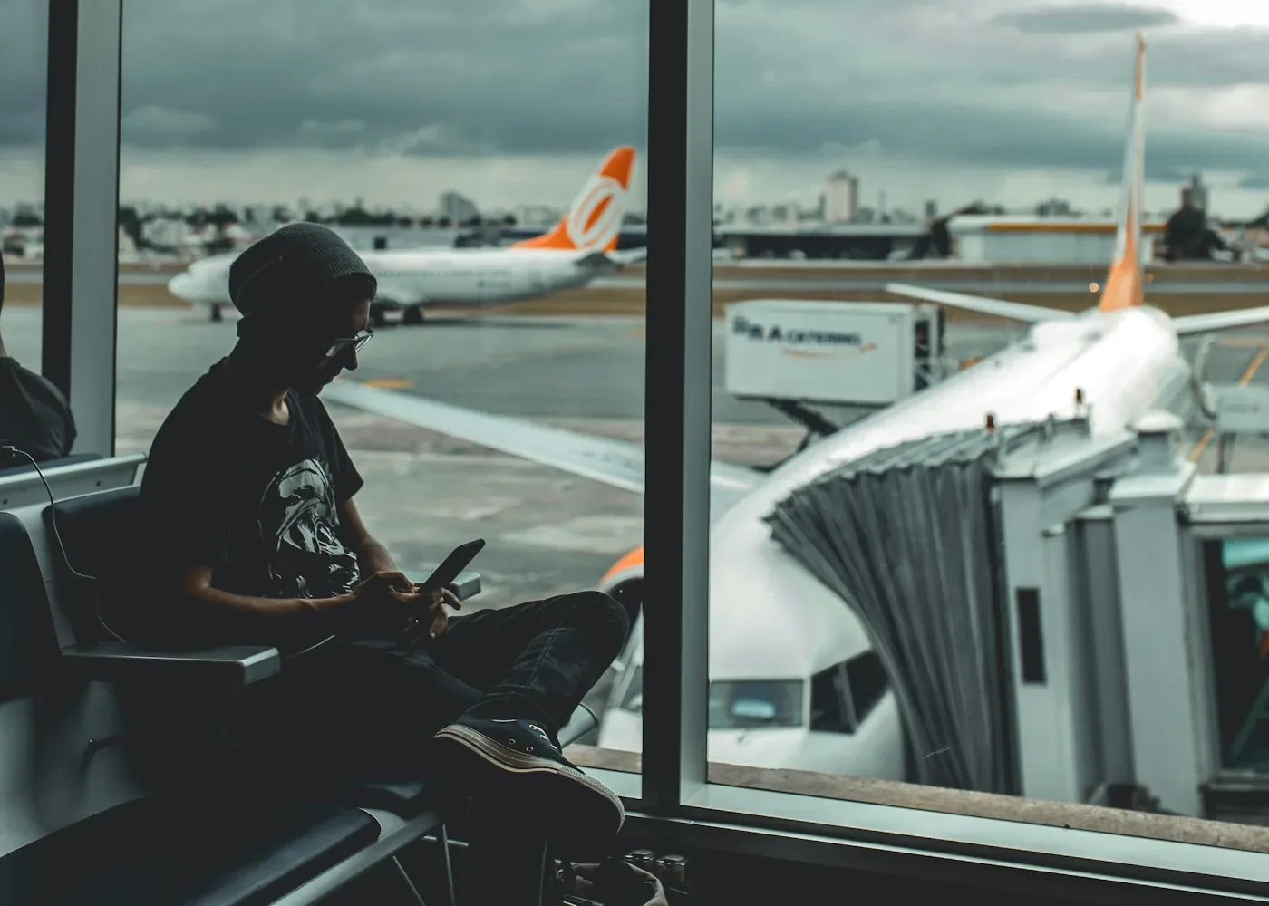 Silhouette of a man sitting by an airport window looking at his phone, with a plane at the gate behind him
