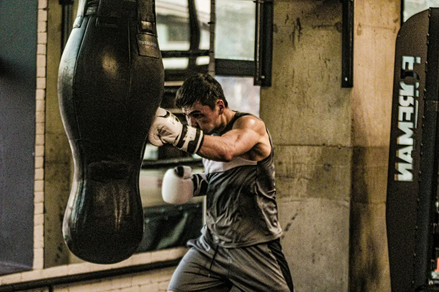 Boxer in a grey vest punching a heavy bag in a boxing gym