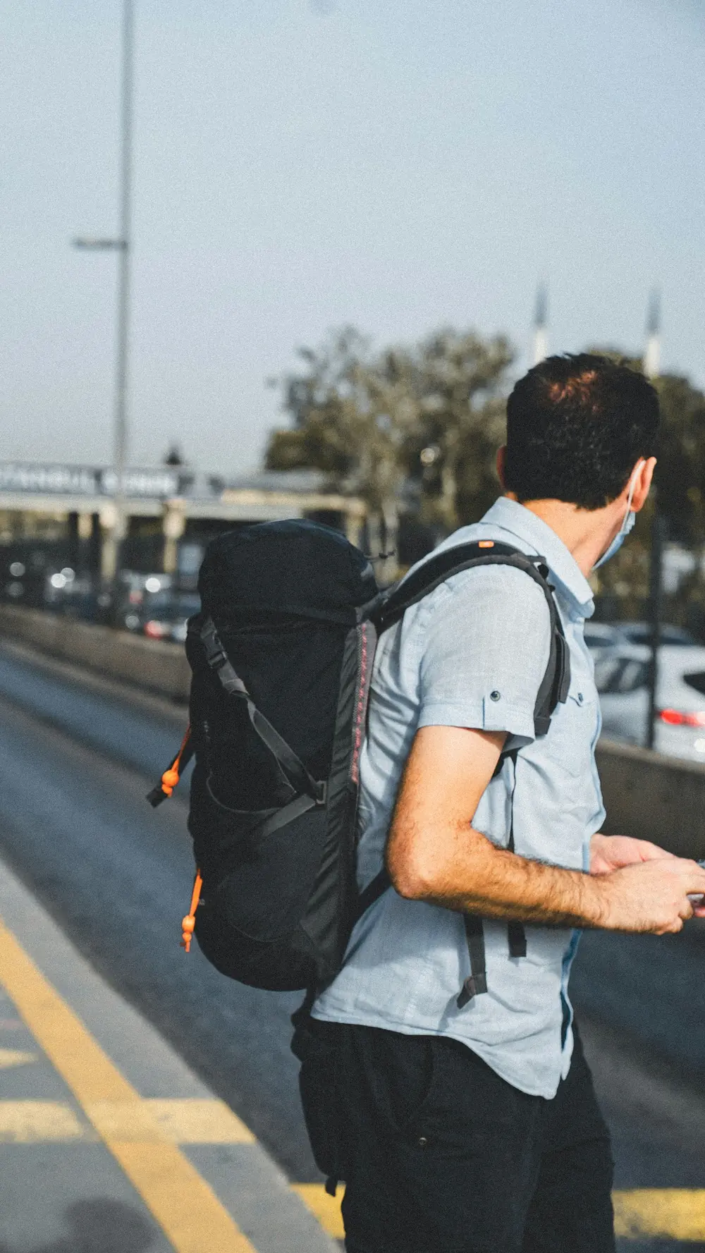 Un hombre con una mochila negra de pie junto a una carretera de la ciudad