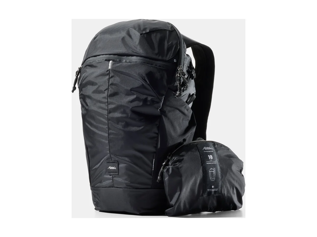 Der Matador 18L Packable Backpack in Schwarz neben seinem Packbeutel