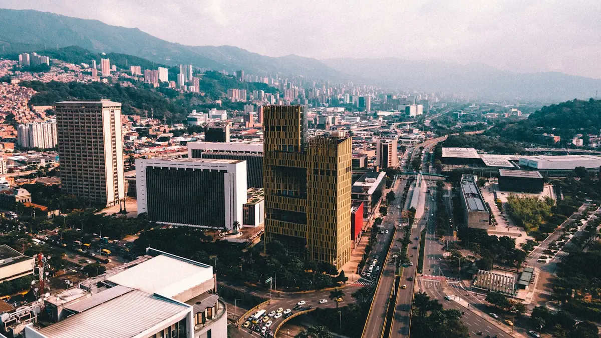 Vista aérea de Medellín con edificios altos, una avenida ancha y colinas verdes detrás