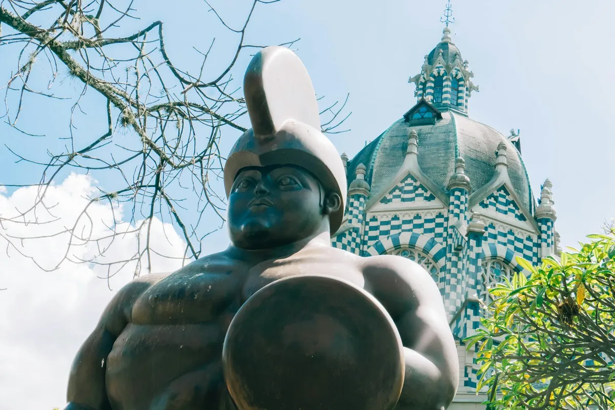 Gran escultura de bronce frente a una cúpula de azulejos verdes y blancos en el centro de Medellín, Colombia