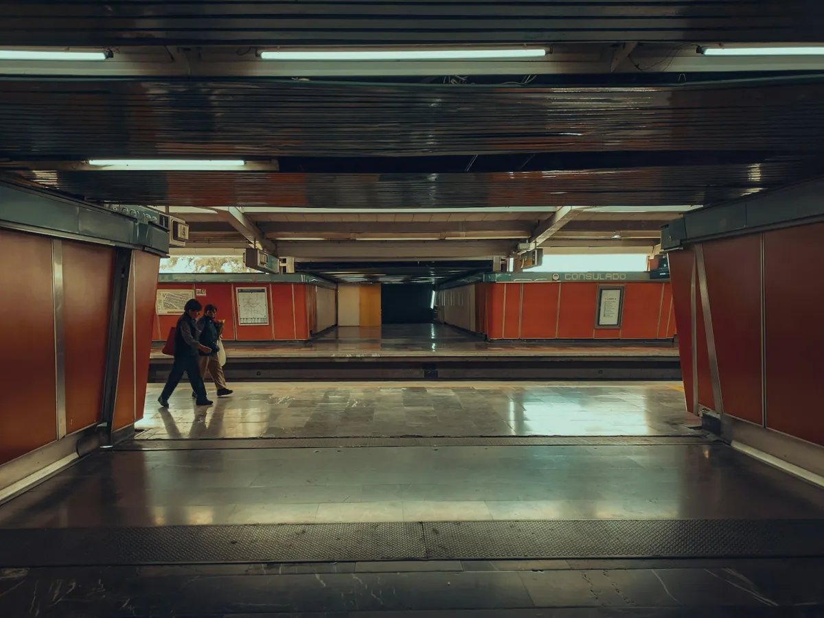 Dos personas caminando por una estación del metro de Ciudad de México con paredes naranjas