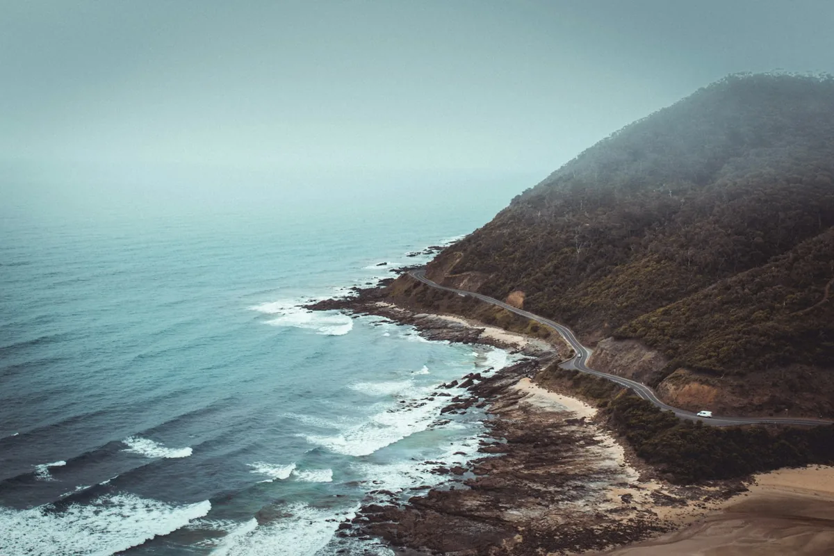 Road curving along a misty headland above a turquoise sea
