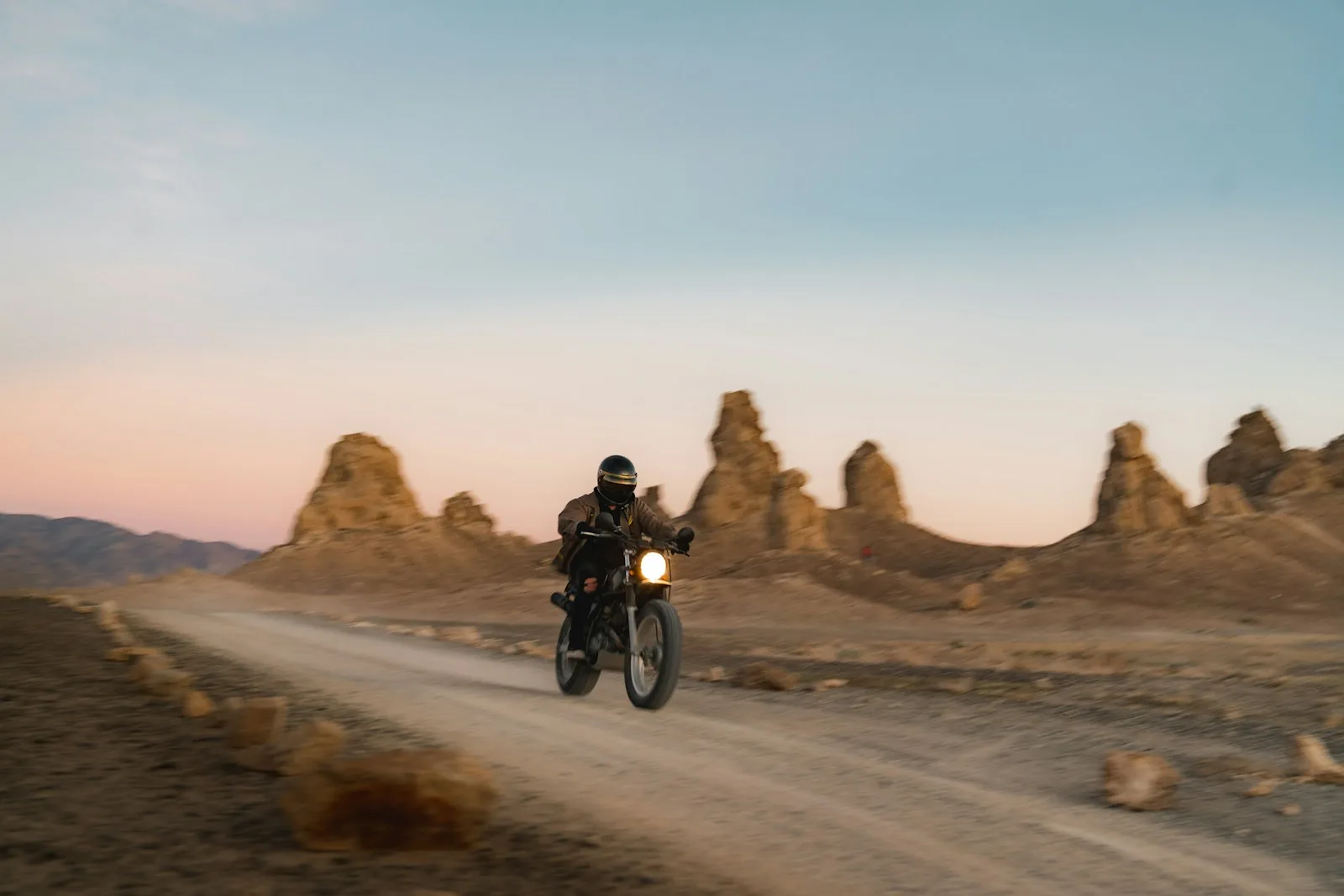 A motorcycle rider on a dirt track through desert rock towers at dusk