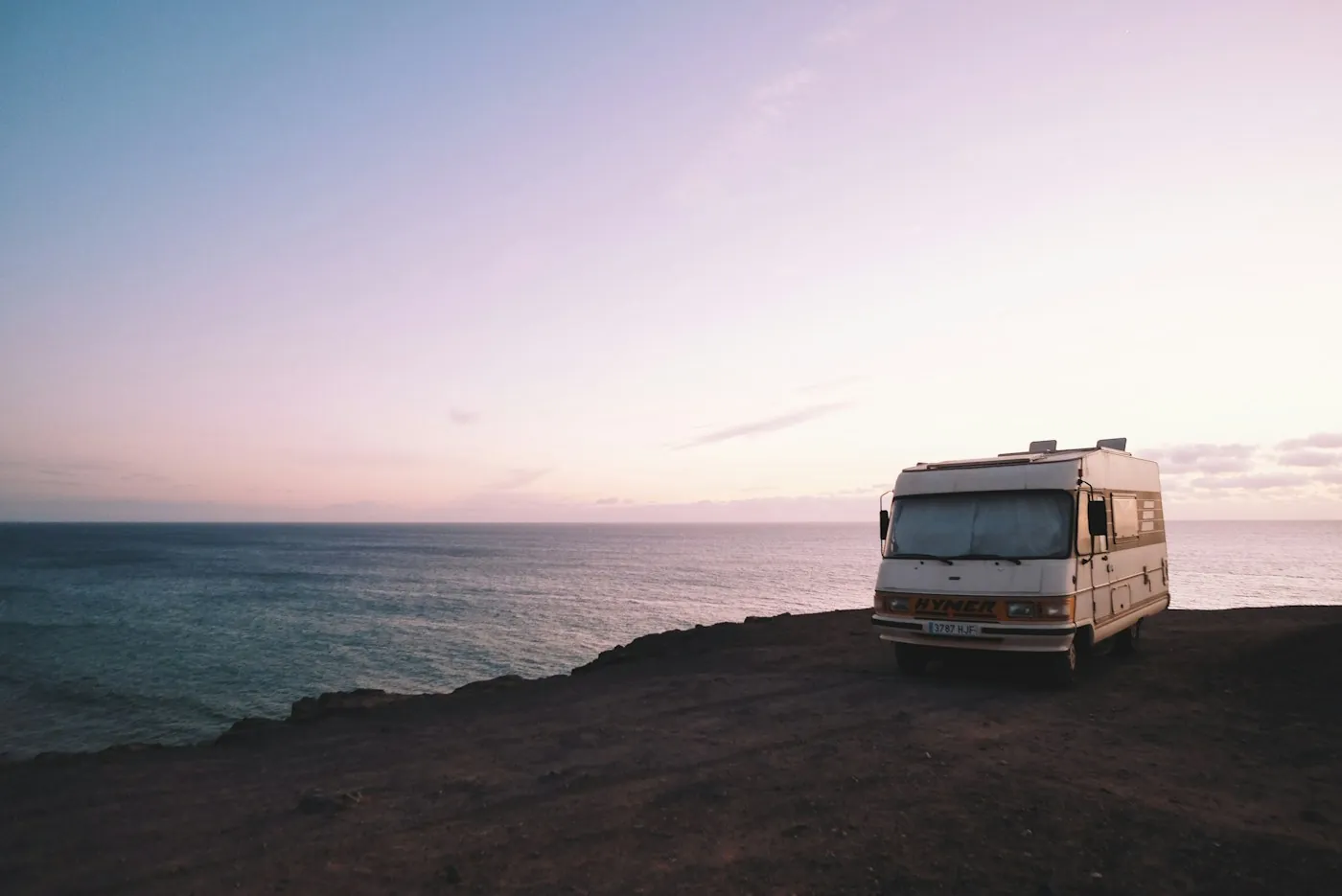 A motorhome parked at the edge of a cliff above the sea at sunset