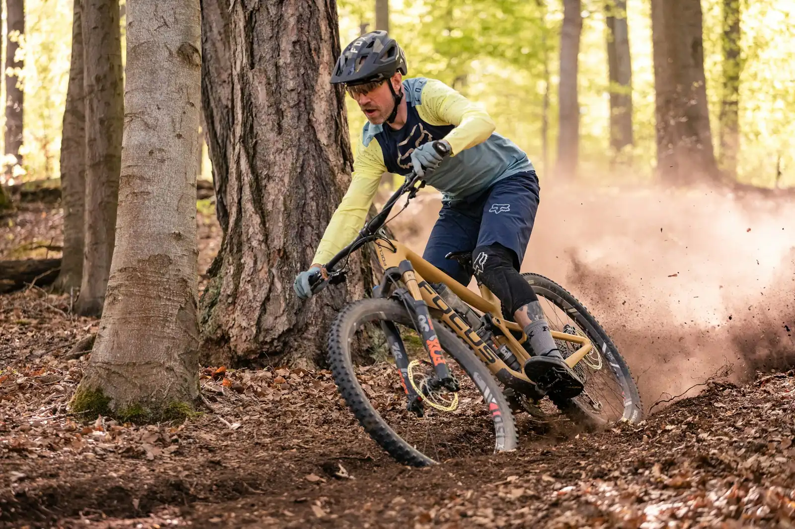 Un ciclista de montaña tomando una curva cerrada en un sendero forestal, con polvo y hojas volando
