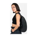 Eine Frau trägt den Nanobag Daypack 16L in Schwarz über einer Schulter