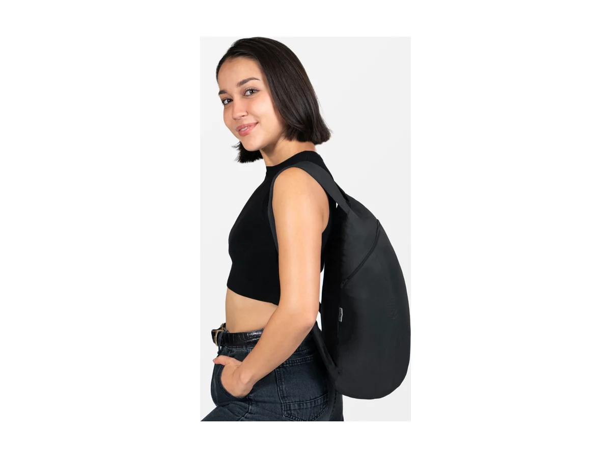 Eine Frau trägt den Nanobag Daypack 16L in Schwarz über einer Schulter