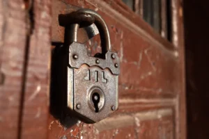 An old iron padlock hanging on a red wooden door