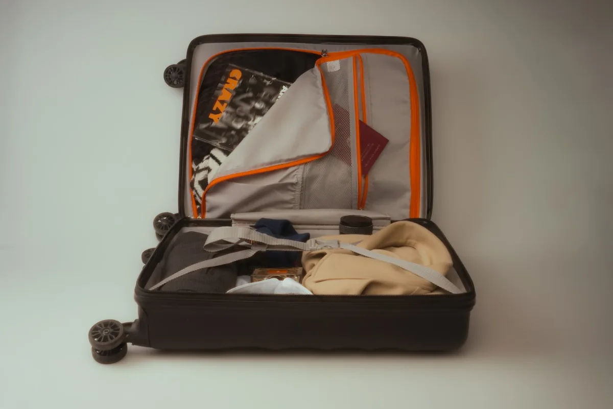 Open black carry-on suitcase packed with clothes on a plain background