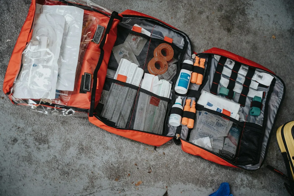 Open orange first aid kit bag with bandages, tape and medical supplies laid out on a grey surface