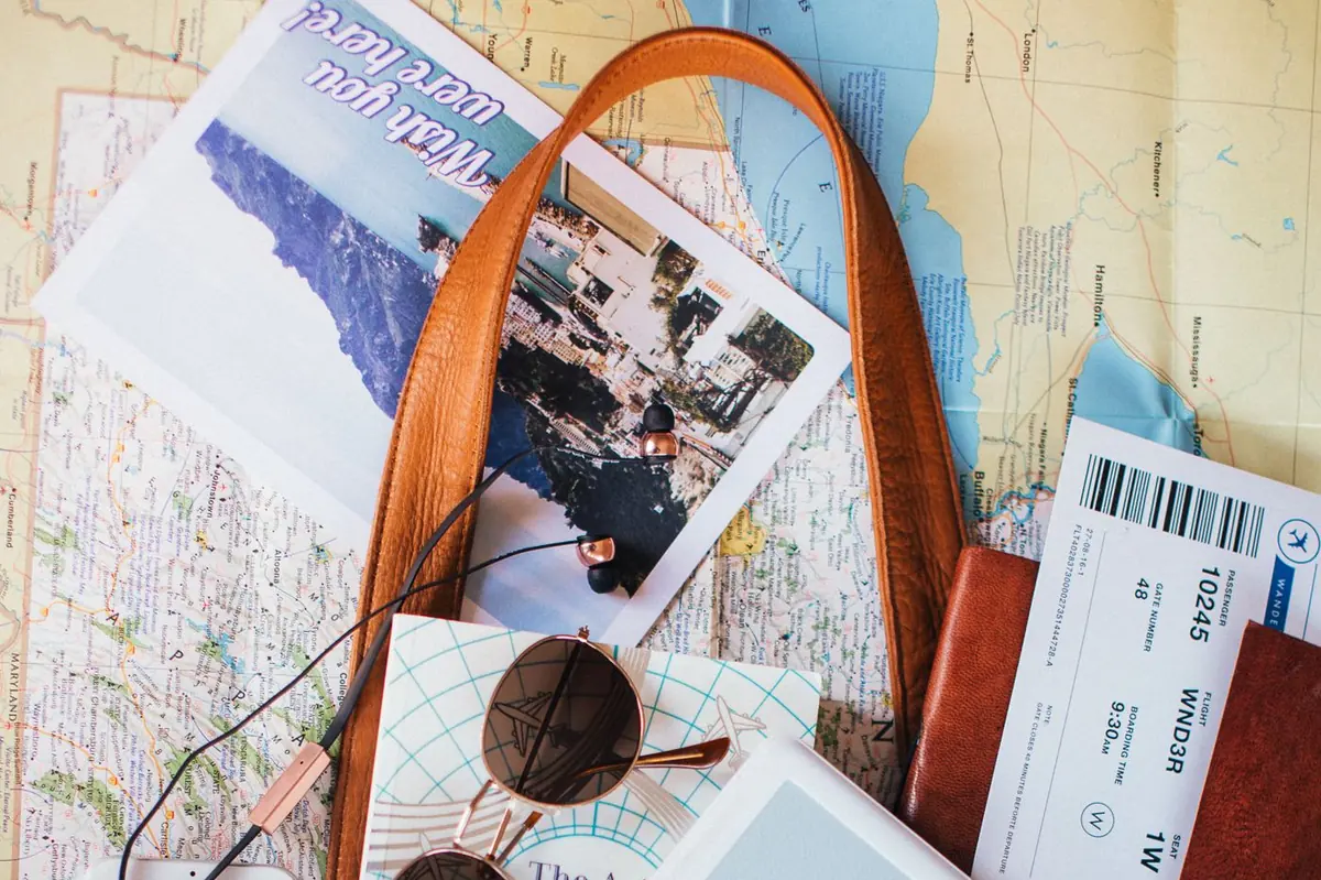 Open leather bag with maps, sunglasses and travel tickets
