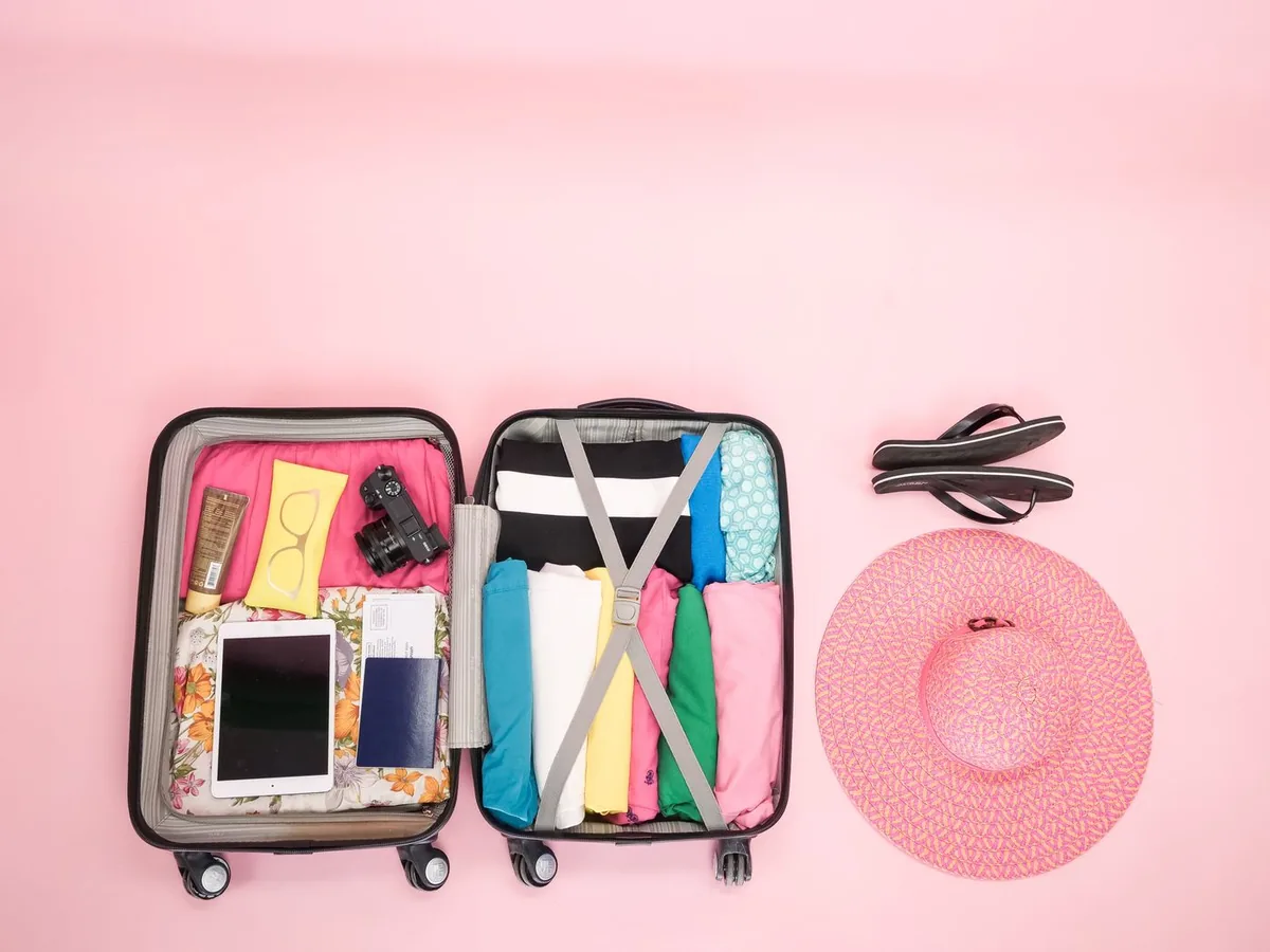 Open suitcase packed neatly with clothes, next to a sun hat and sandals