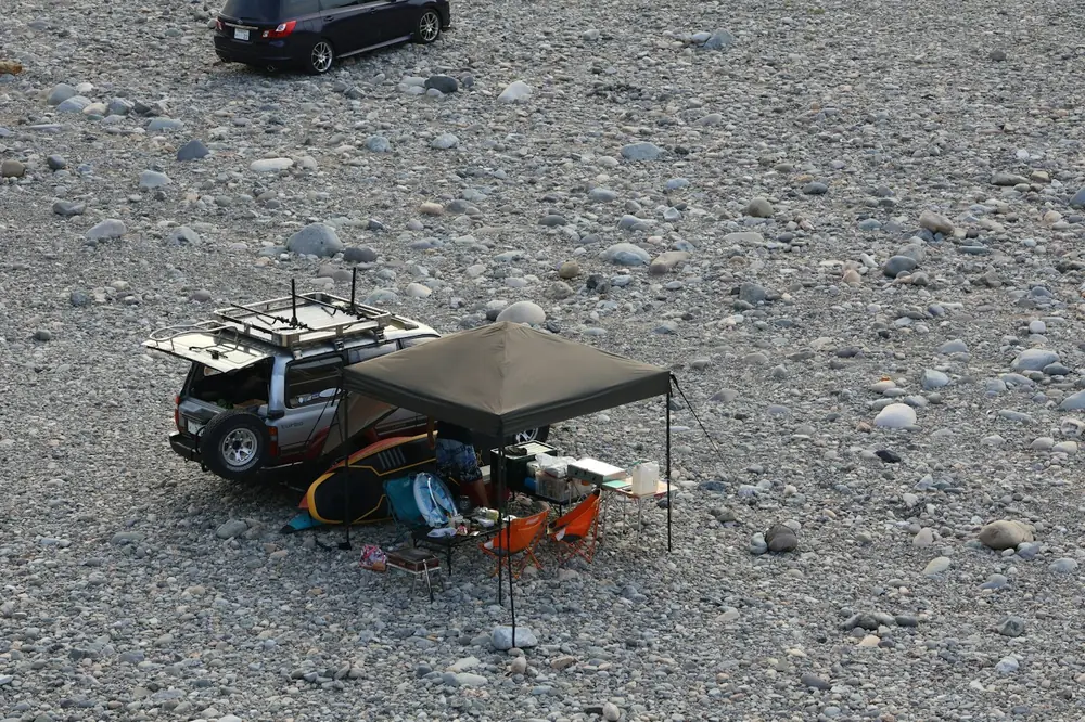 Overland camp seen from above with a 4x4, a shade awning and gear laid out on rocky ground