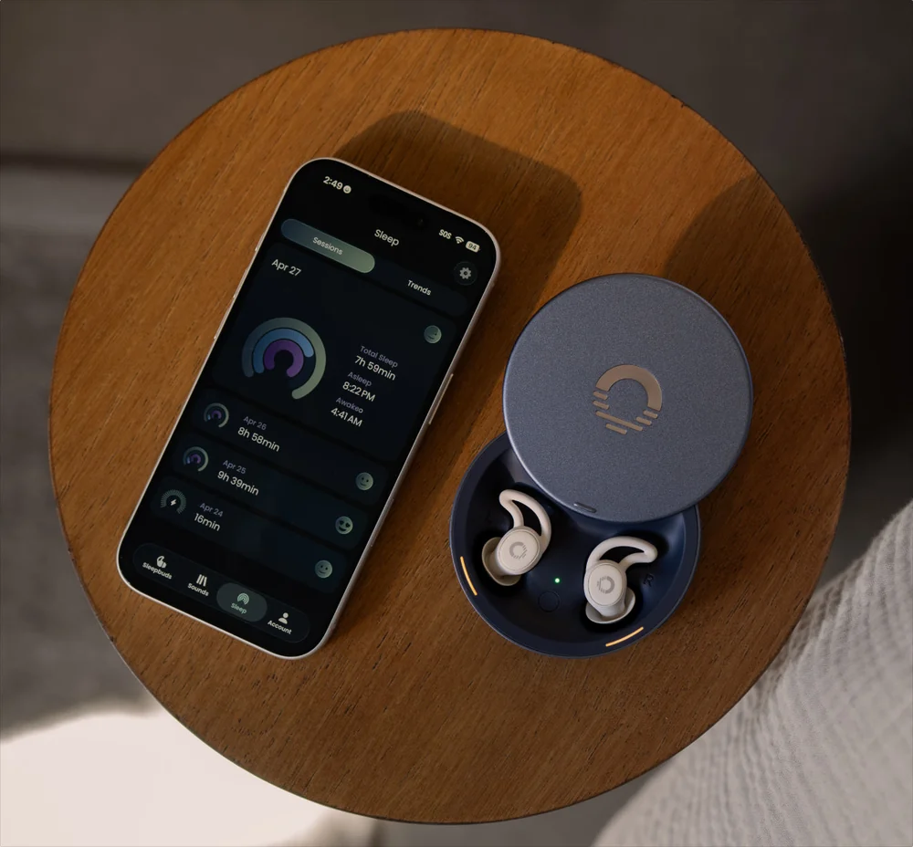 Phone showing the Ozlo sleep app next to the open Ozlo Sleepbuds 2 case on a round wooden table