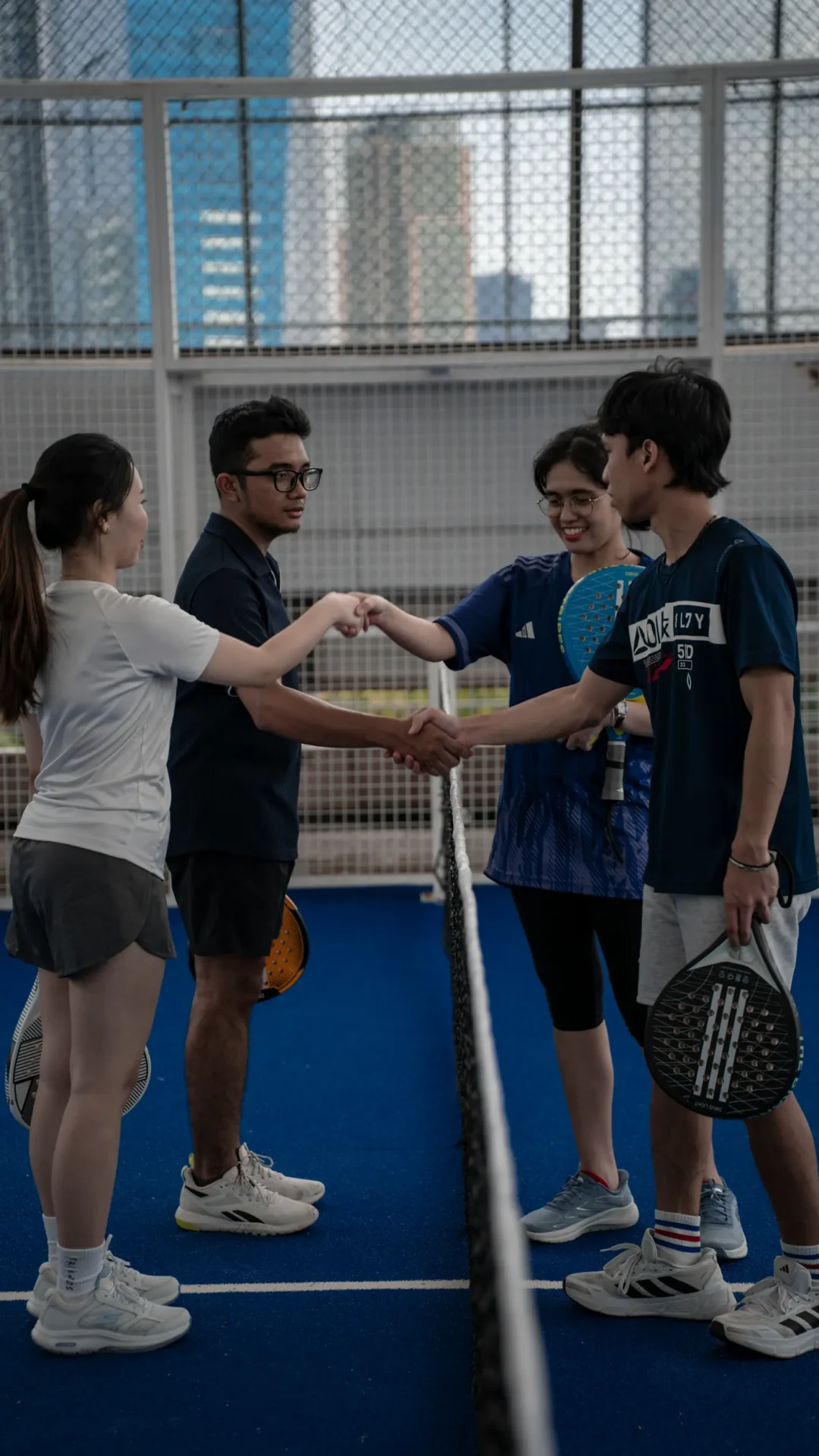Four padel players fist-bumping and shaking hands at the net