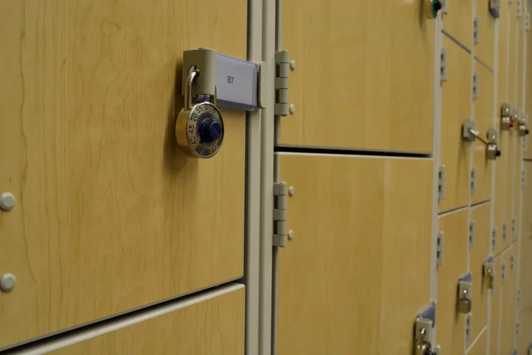 Combination padlock hanging through the latch of a wooden locker door, with more lockers beside it