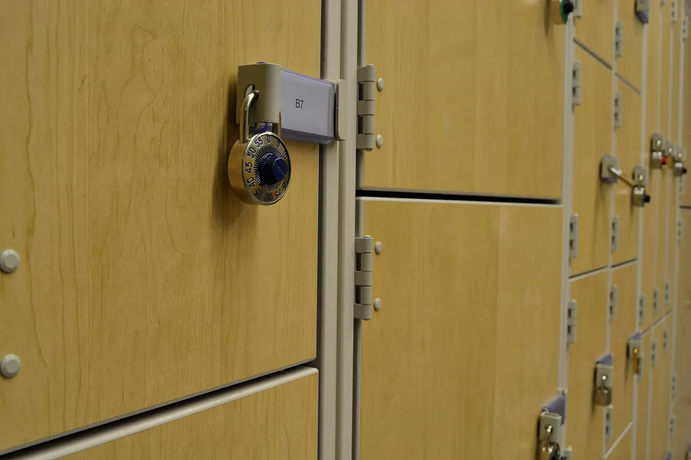 Combination padlock hanging through the latch of a wooden locker door, with more lockers beside it