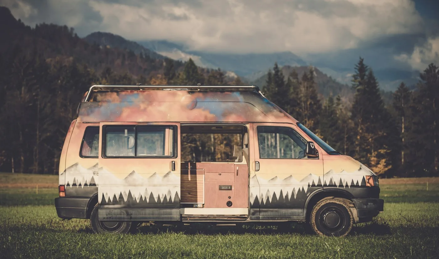 Painted camper van parked in a meadow with forested mountains behind it