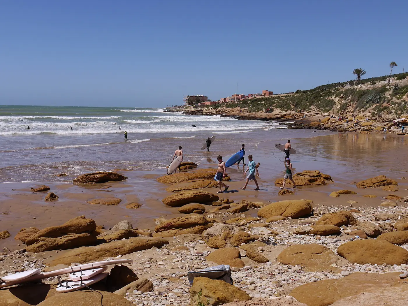 Surfers carrying boards across rocks to the water at Panorama beach in Taghazout, Morocco