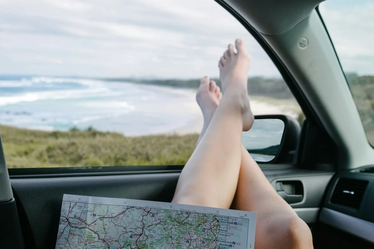 Een passagier met voeten op het dashboard die een papieren kaart vasthoudt dicht bij de kust