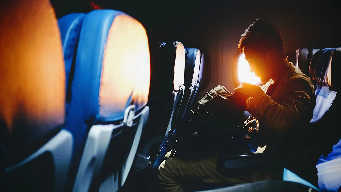 Passenger in an airplane window seat with a backpack and the sun coming through the window