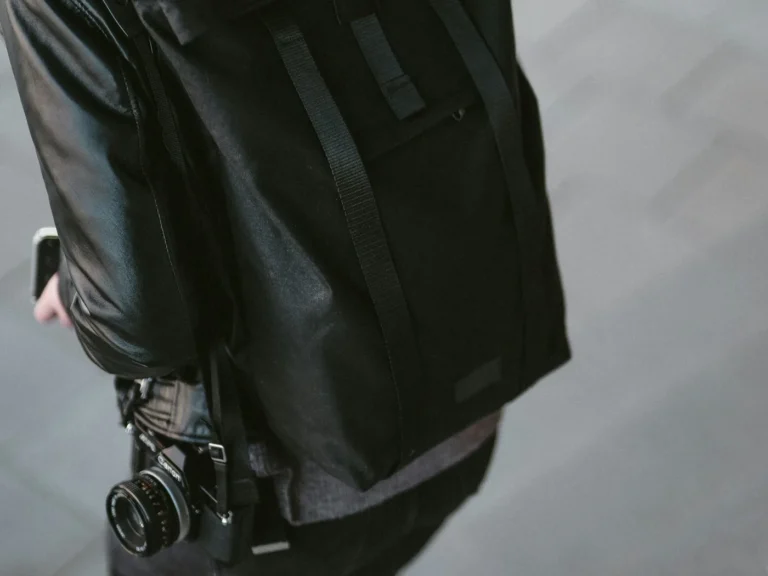 Woman with a black roll-top backpack and a film camera hanging at her side