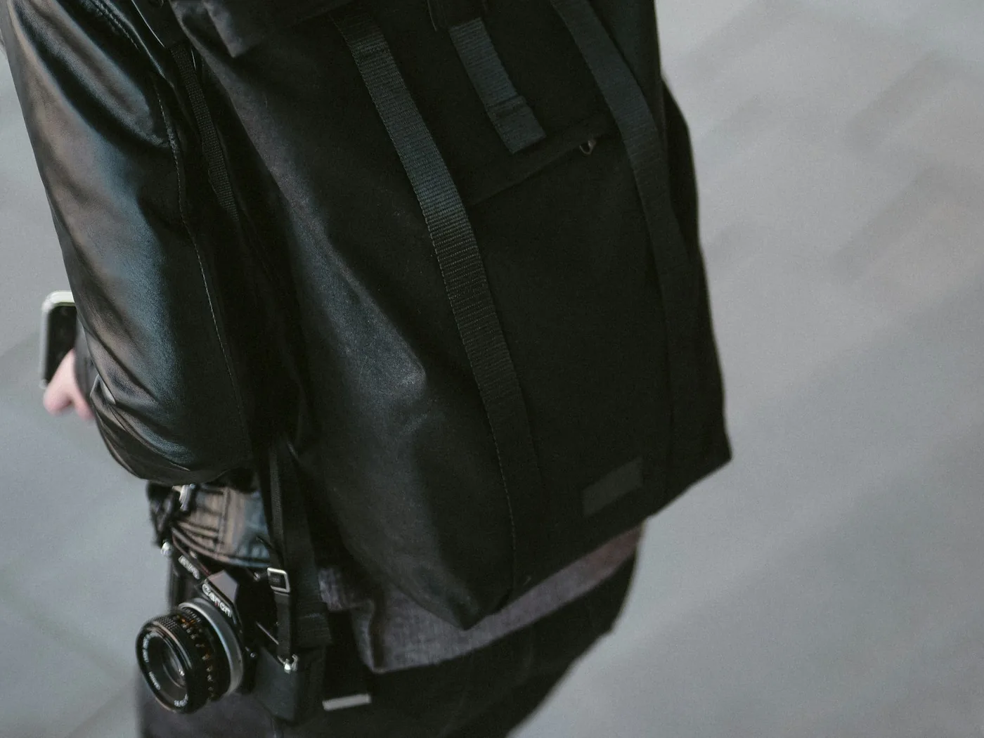 Woman with a black roll-top backpack and a film camera hanging at her side
